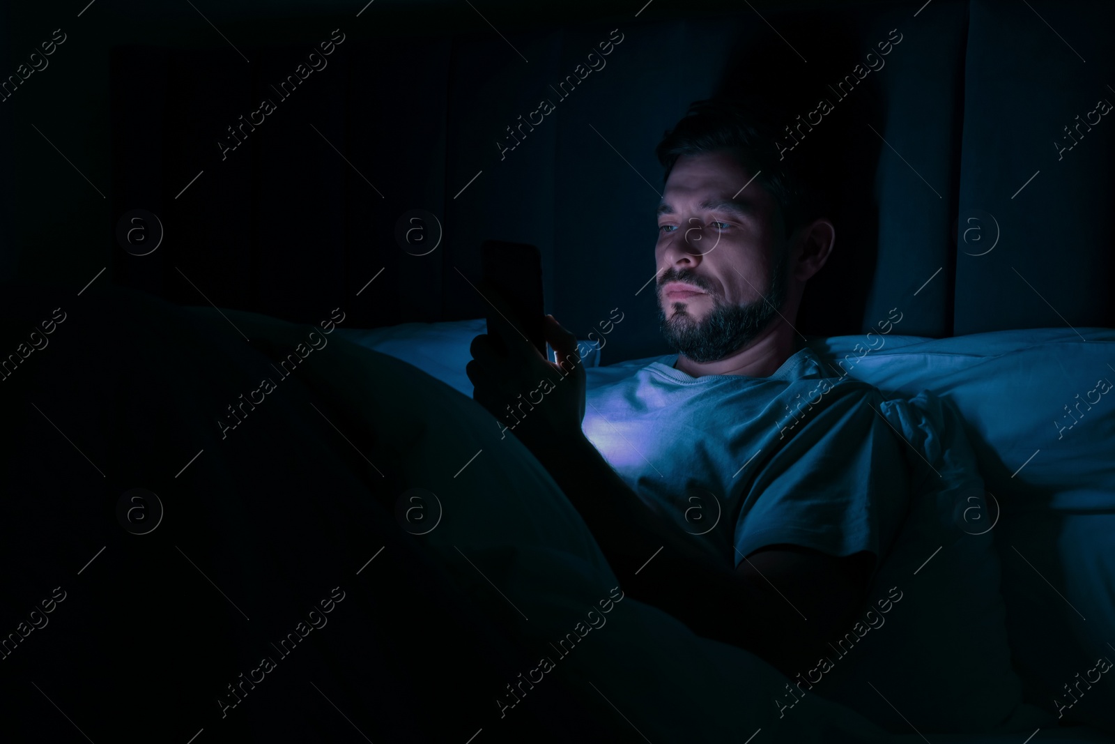 Photo of Man using smartphone in bed at night. Internet addiction