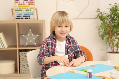 Photo of Cute little boy using glue stick at desk in room. Home workplace