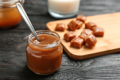 Jar with tasty caramel sauce and spoon on wooden table. Space for text