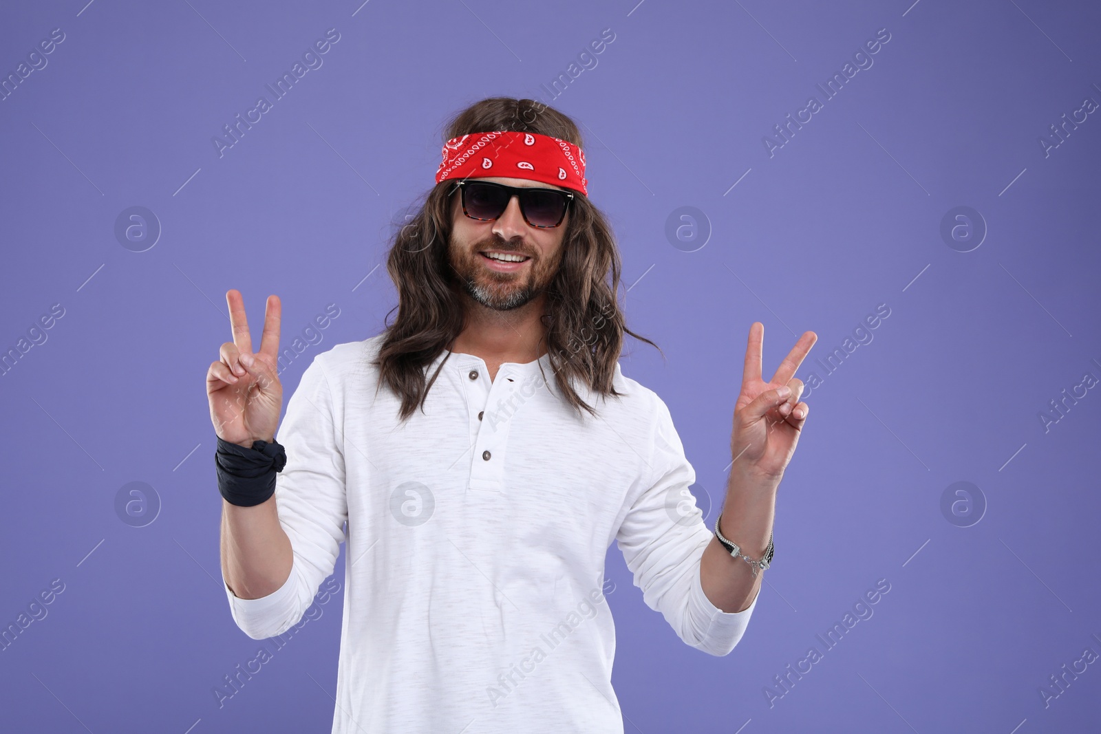 Photo of Stylish hippie man in sunglasses showing V-sign on violet background