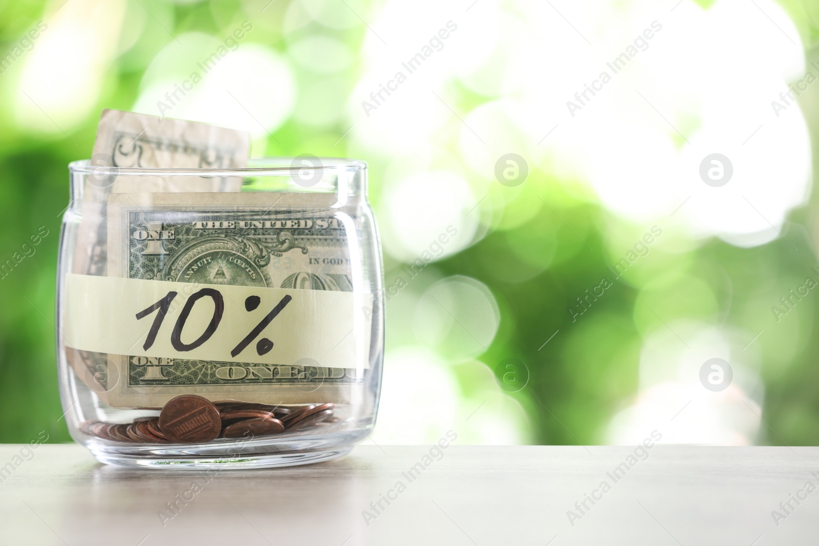 Photo of Glass jar with money and label 10 PERCENT on table against blurred background. Space for text