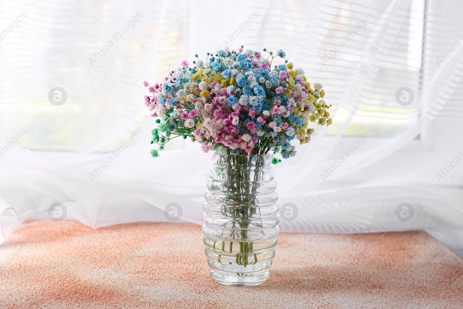 Photo of Beautiful gypsophila flowers in vase on textured table near window