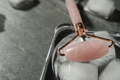 Photo of Natural jade face roller and ice cubes on grey background, closeup