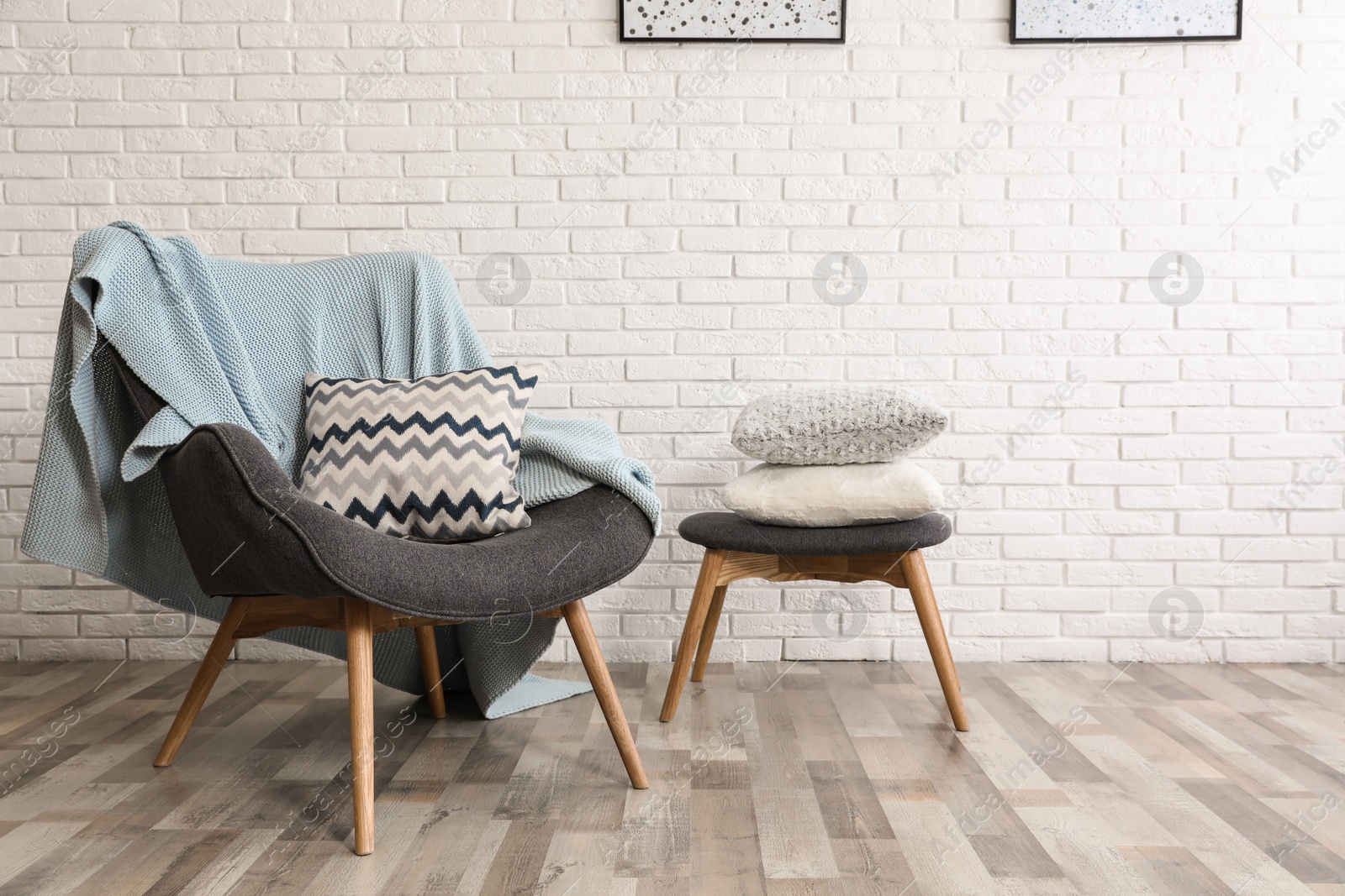 Photo of Stylish interior with plaid, pillows and armchair near brick wall, space for text