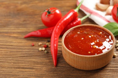 Photo of Spicy chili sauce and ingredients on wooden table, space for text