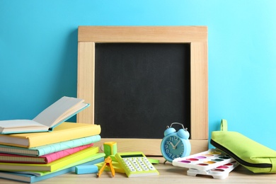 Photo of Different school stationery and small blank chalkboard on table near light blue wall. Space for text