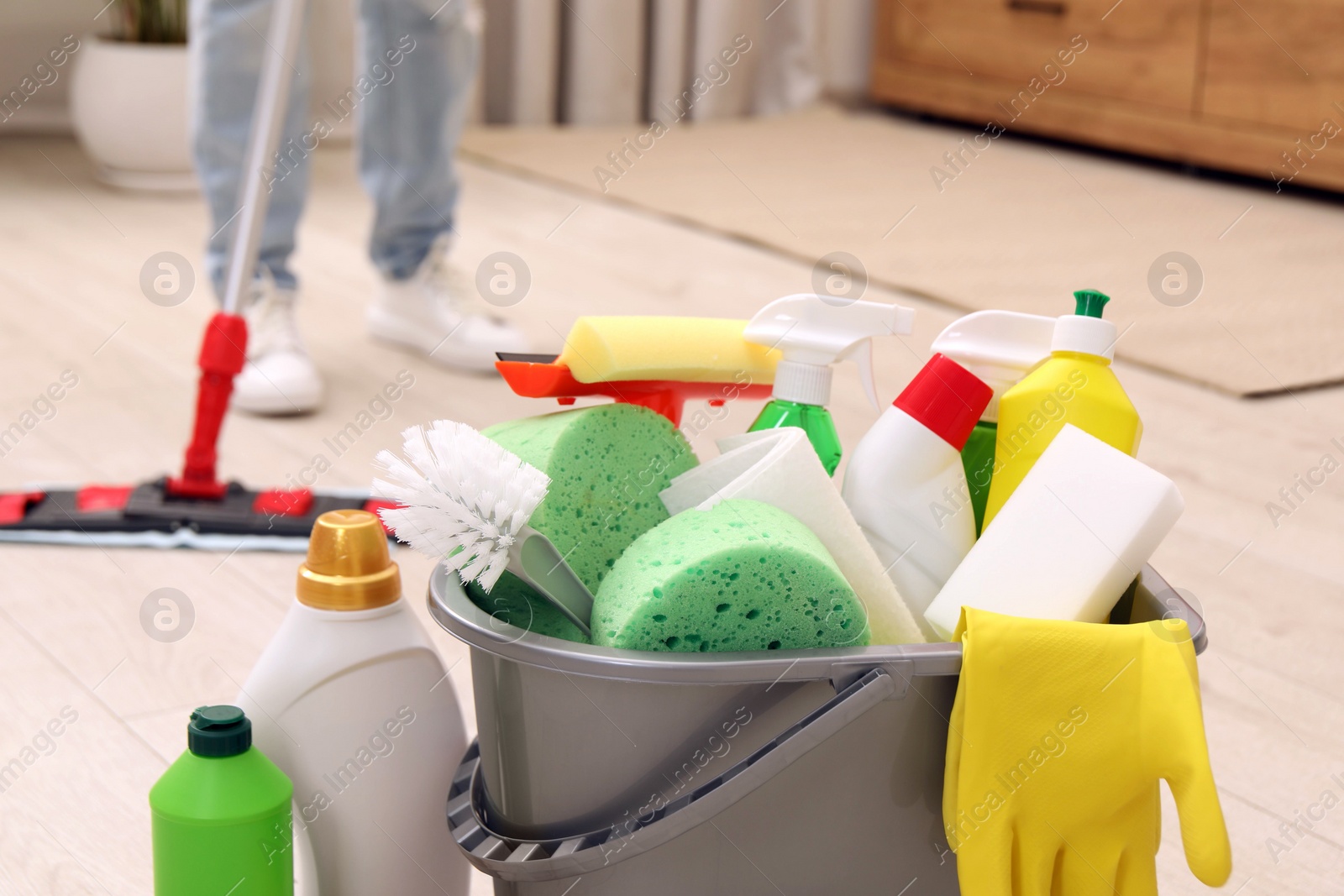 Photo of Different cleaning supplies in bucket and woman mopping floor, selective focus