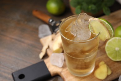 Photo of Glass of tasty ginger ale with ice cubes and ingredients on wooden table, closeup. Space for text