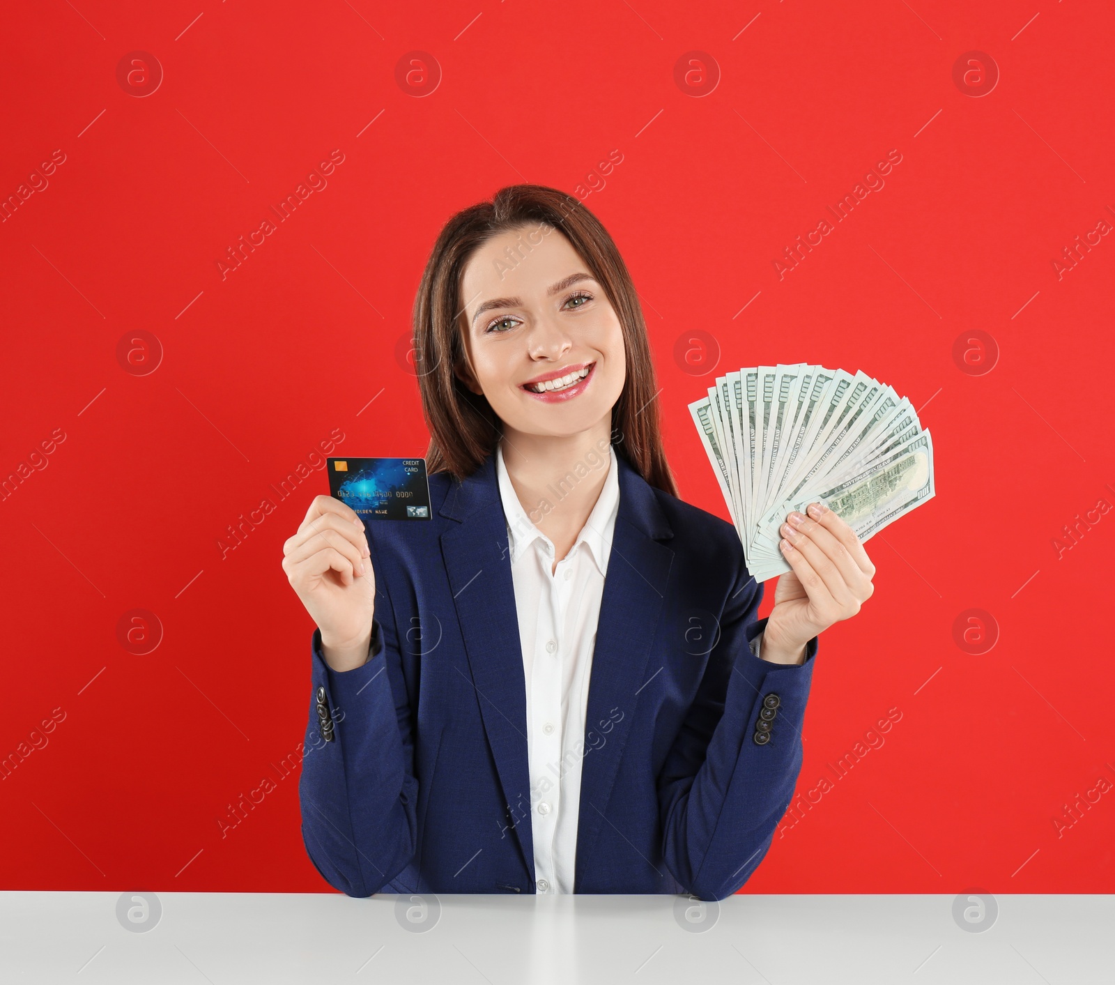 Photo of Young woman with money and credit card at table on crimson background
