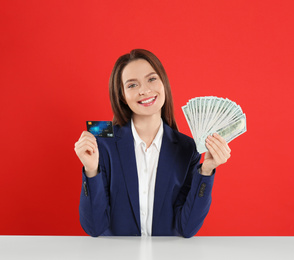 Photo of Young woman with money and credit card at table on crimson background