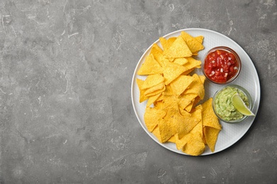 Plate with delicious mexican nachos chips and sauces on grey table, top view. Space for text