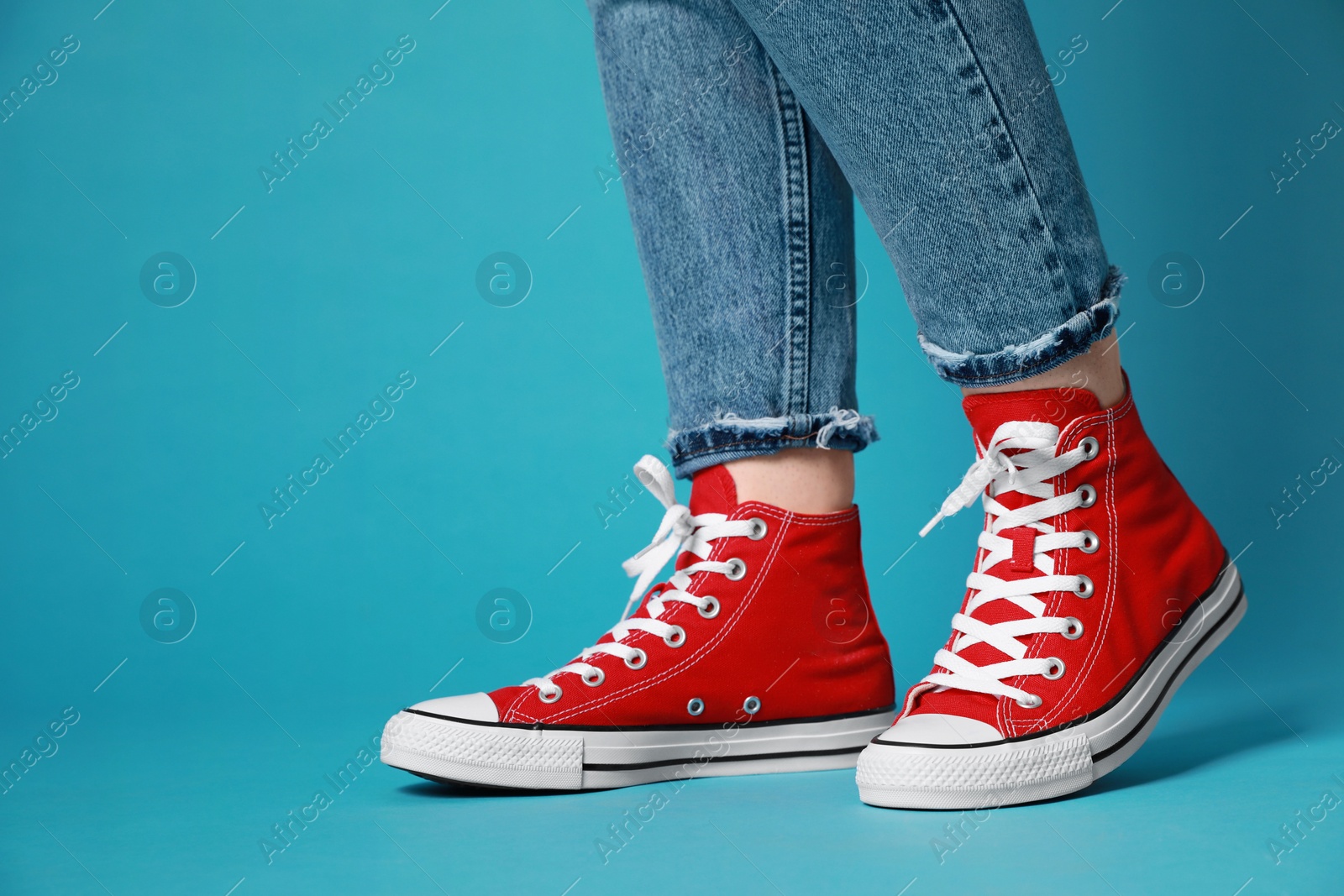 Photo of Woman wearing pair of new stylish sneakers on light blue background, closeup