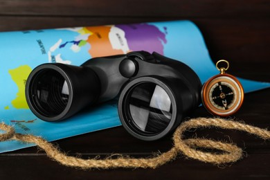 Photo of Modern binoculars, rope, compass and map on wooden table, closeup