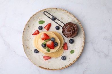 Photo of Delicious pancakes served with berries and chocolate spread on white marble table, top view