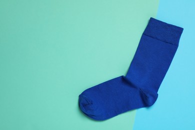 Photo of New blue sock on color background, top view. Space for text