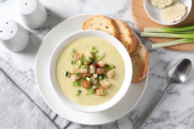 Photo of Tasty potato soup with croutons and green onion in bowl served on white marble table, flat lay