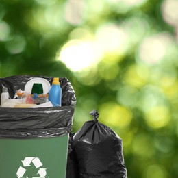 Image of Waste bin and plastic bags full of garbage on blurred background, space for text