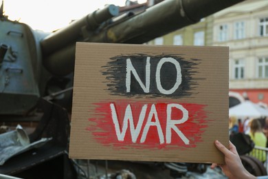 Photo of Woman holding poster with words No War near broken military tank on street, closeup