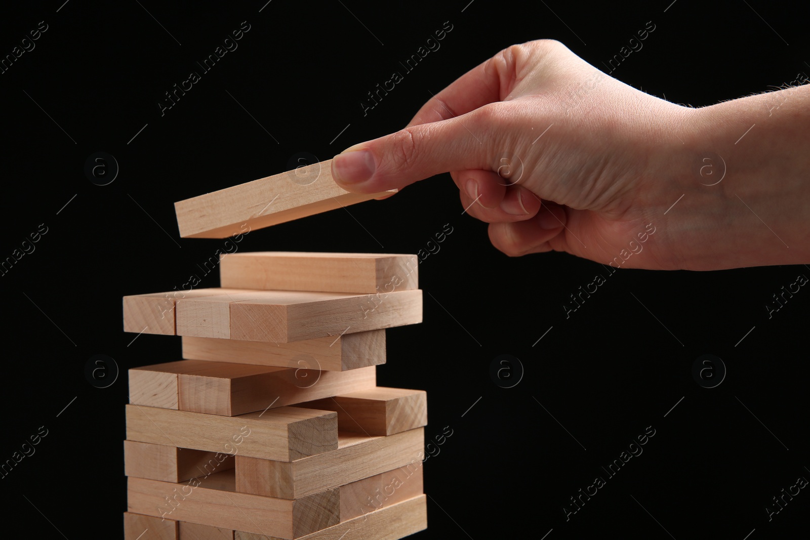 Photo of Woman playing Jenga on black background, closeup