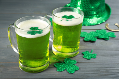 Photo of Green beer and clover leaves on grey wooden table. St. Patrick's Day celebration