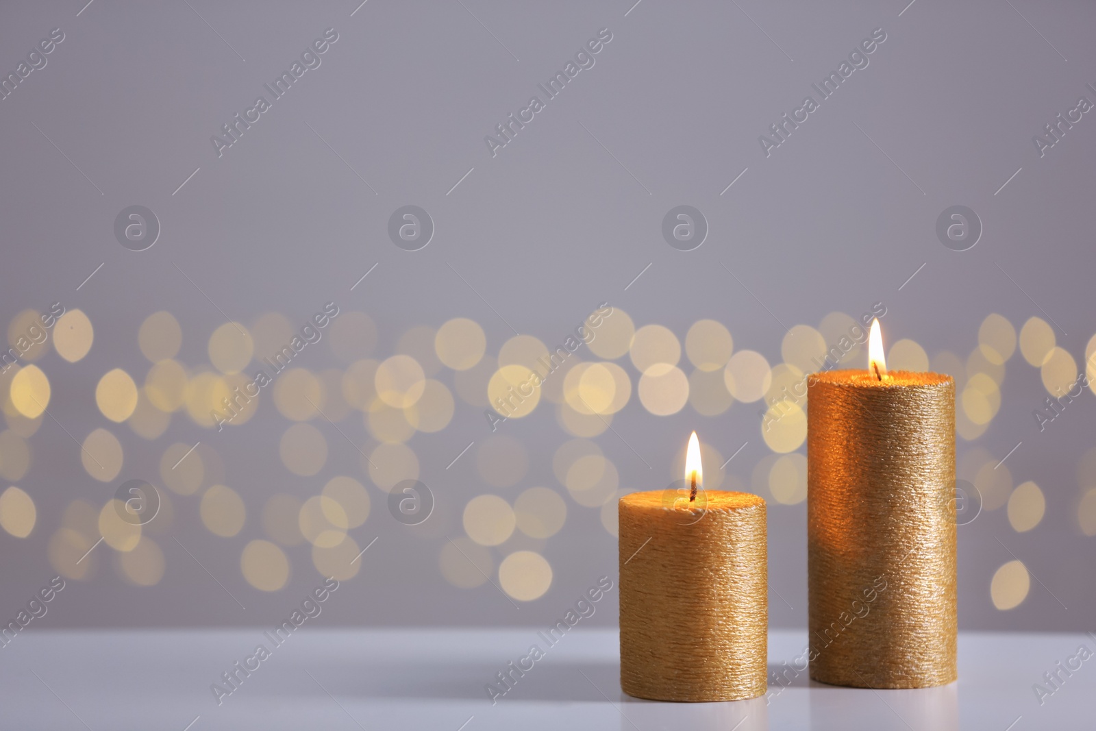 Photo of Burning gold candles on table against blurred lights. Space for text