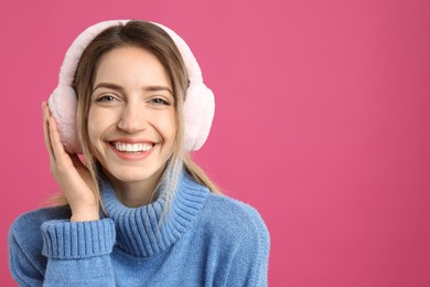 Happy woman wearing warm earmuffs on pink background, space for text