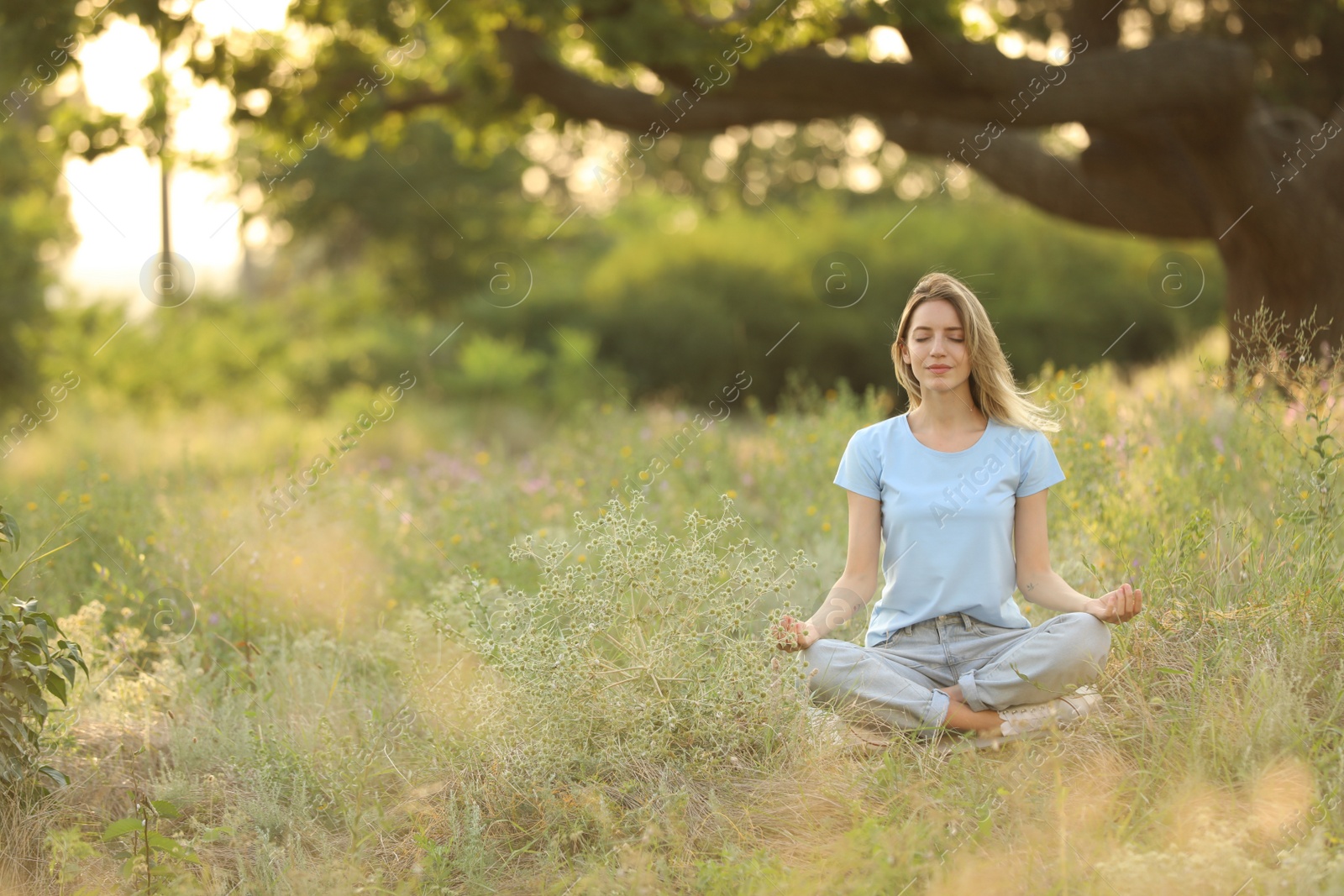 Photo of Young woman meditating on green grass in park, space for text