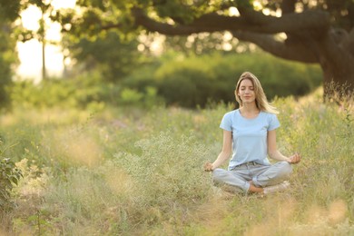 Photo of Young woman meditating on green grass in park, space for text