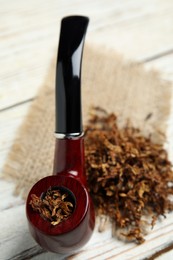 Photo of Smoking pipe and dry tobacco on white wooden table, closeup