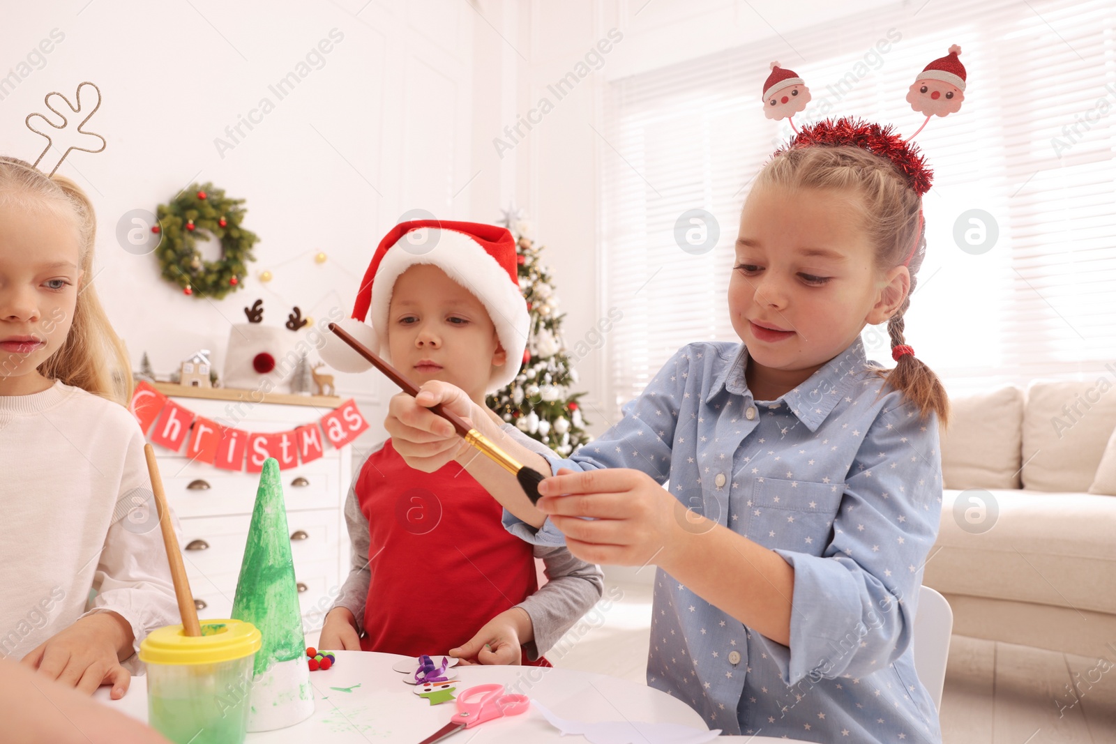 Photo of Cute little children making Christmas crafts at table in decorated room