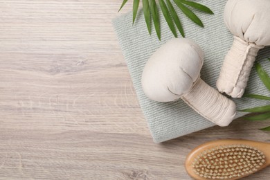 Beautiful spa composition with herbal massage bags and green leaves on light wooden table, flat lay. Space for text