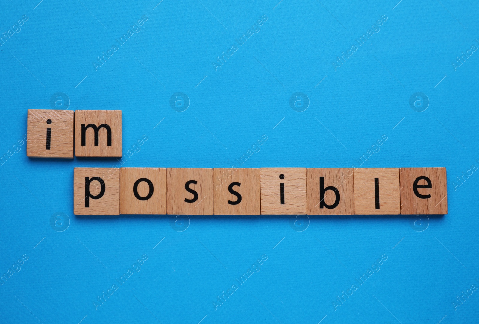 Photo of Motivation concept. Changing word from Impossible into Possible by removing wooden squares on light blue background, flat lay