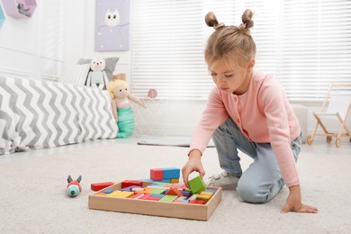 Photo of Cute little girl playing with colorful building blocks at home