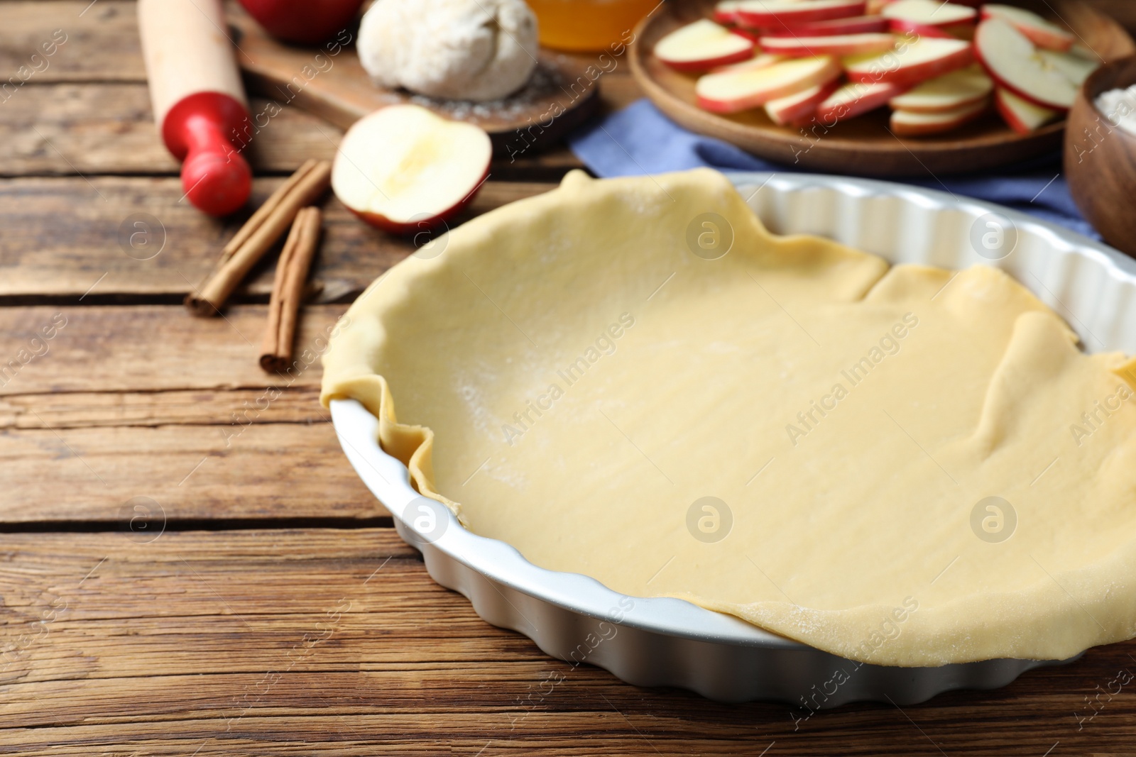 Photo of Baking dish with raw dough for apple pie and ingredients on wooden table