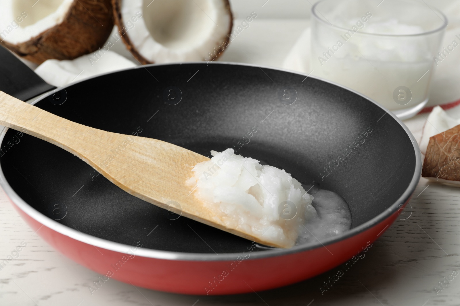 Photo of Frying pan with coconut oil and wooden spatula on white wooden table, closeup. Healthy cooking