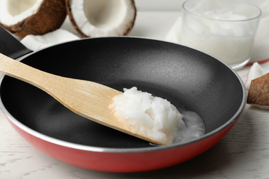 Photo of Frying pan with coconut oil and wooden spatula on white wooden table, closeup. Healthy cooking