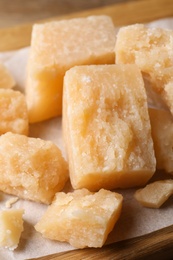 Photo of Pieces of delicious parmesan cheese on parchment, closeup view