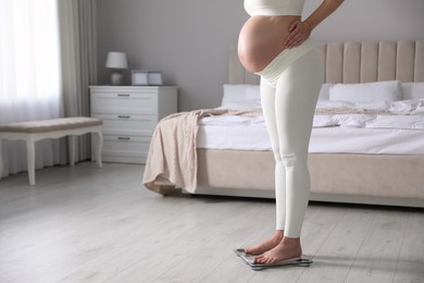 Pregnant woman standing on scales in bedroom, closeup. Space for text