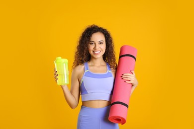 Beautiful African American woman with yoga mat and shaker on yellow background