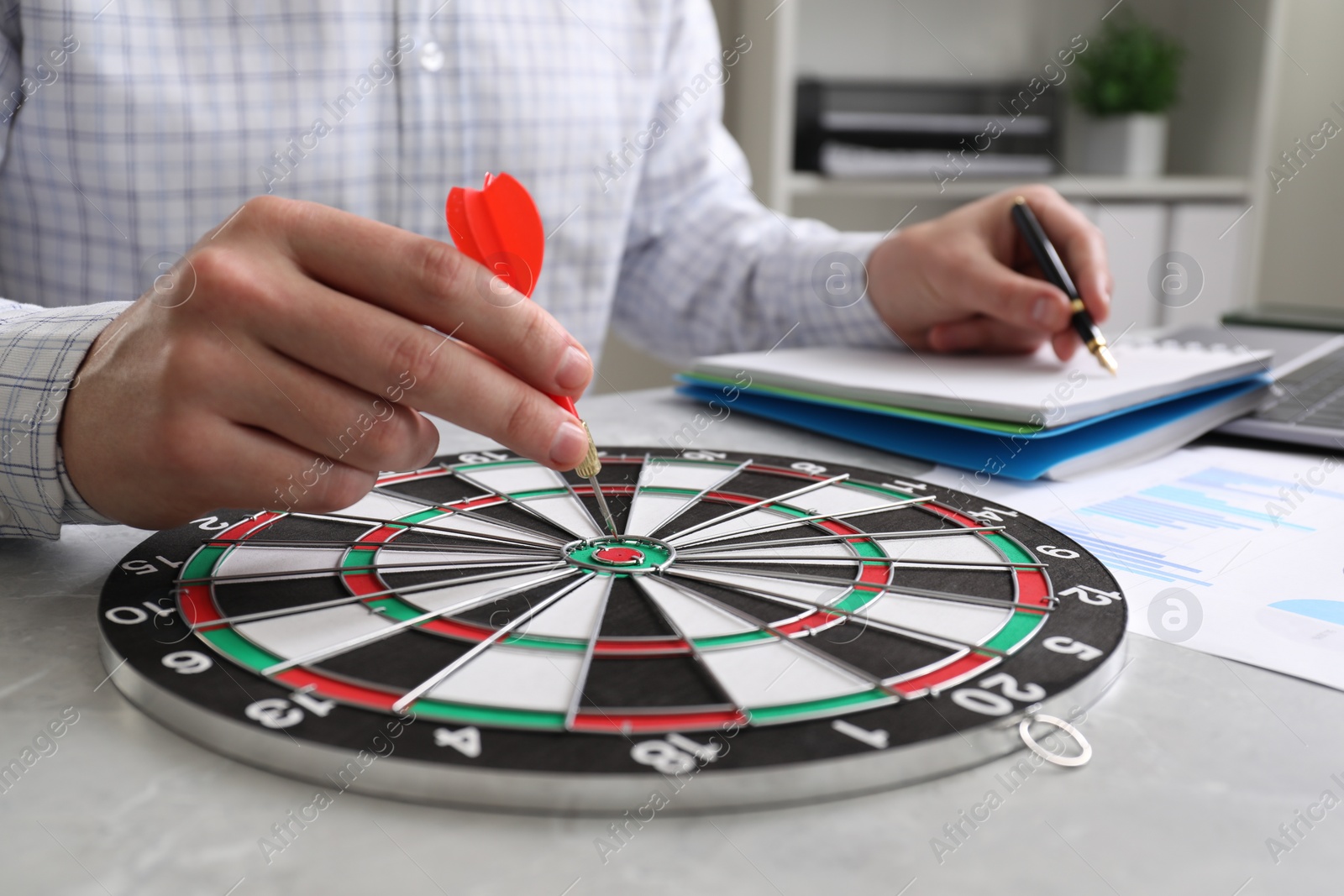 Photo of Business targeting concept. Man with dart aiming at dartboard at gray table indoors, closeup