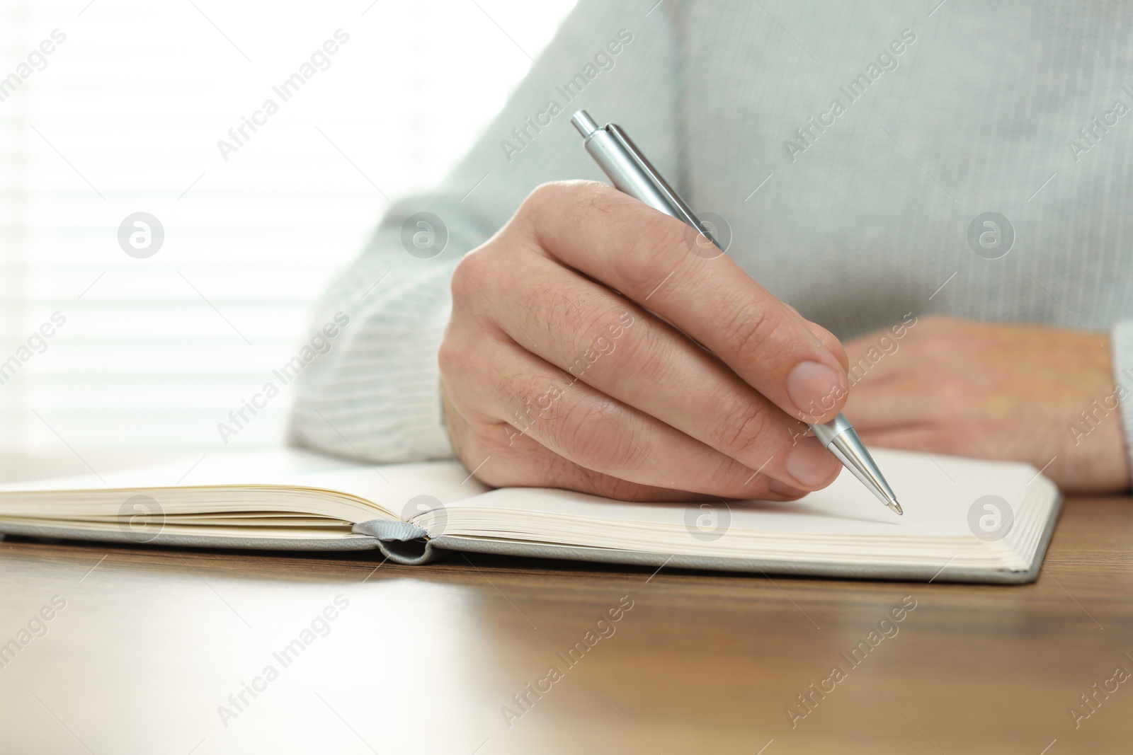 Photo of Man writing in notebook at wooden table, closeup