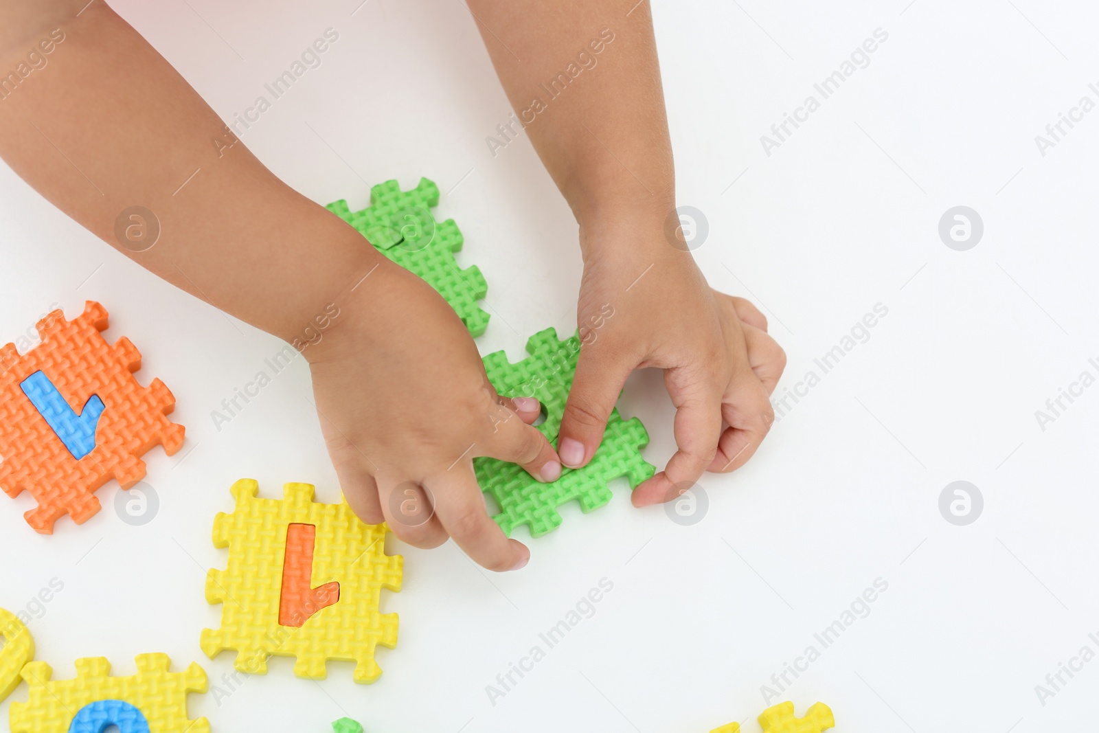 Photo of Little girl playing with colorful puzzles at white table, top view. Educational toy