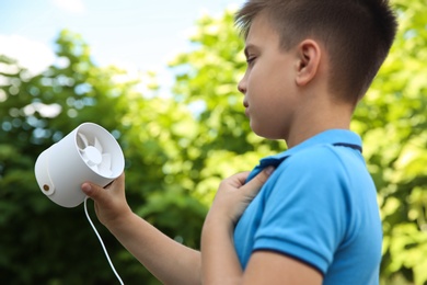 Photo of Little boy with portable fan outdoors. Summer heat