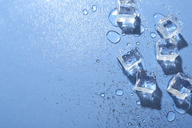 Melting ice cubes and water drops on blue background, flat lay. Space for text