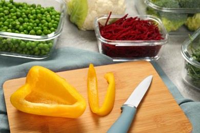 Photo of Cut bell pepper, knife and containers with fresh products on light gray table. Food storage
