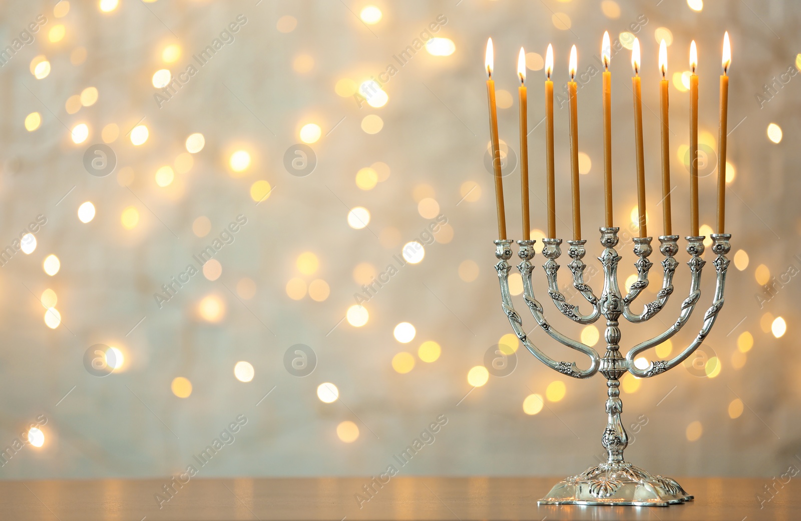 Photo of Hanukkah menorah with candles on table against blurred lights