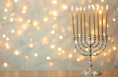 Hanukkah menorah with candles on table against blurred lights