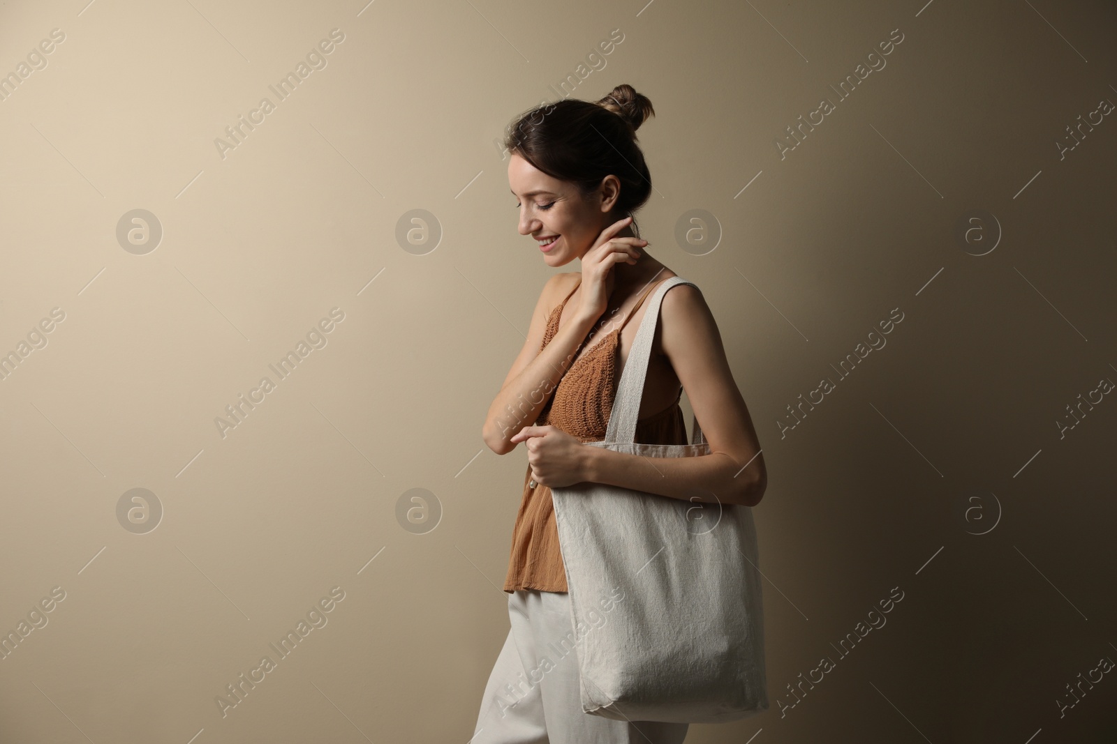 Photo of Happy young woman with blank eco friendly bag against beige background