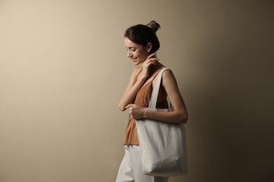 Happy young woman with blank eco friendly bag against beige background