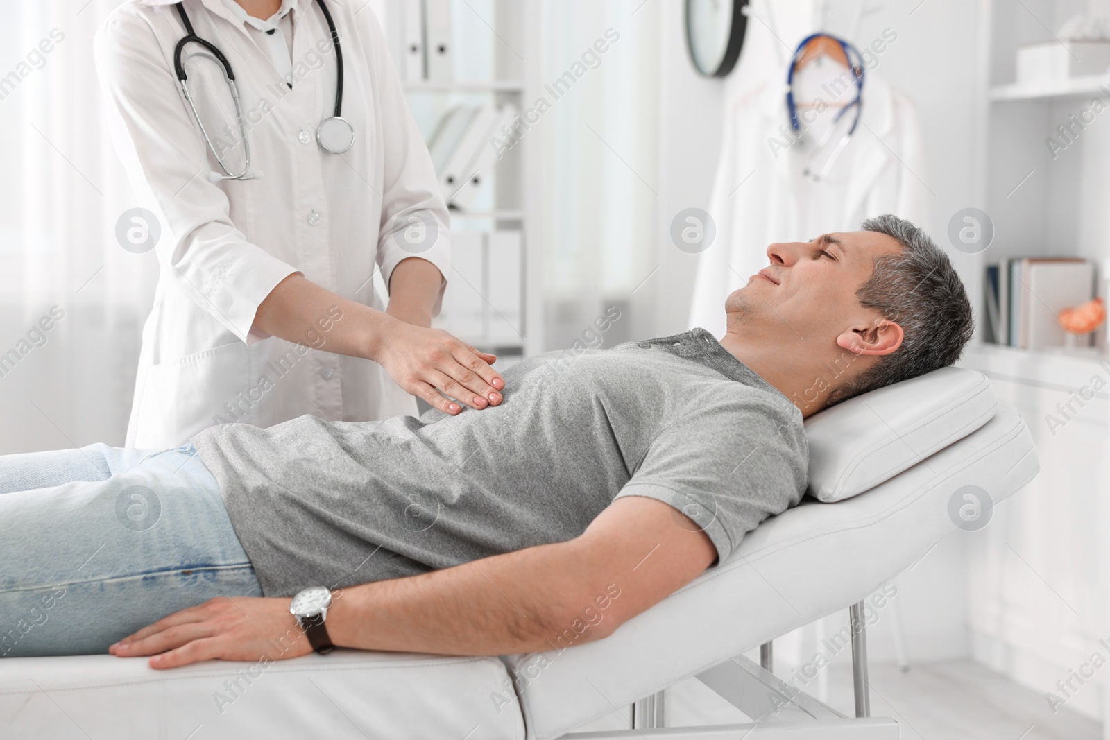 Photo of Gastroenterologist examining patient with stomach pain on couch in clinic, closeup